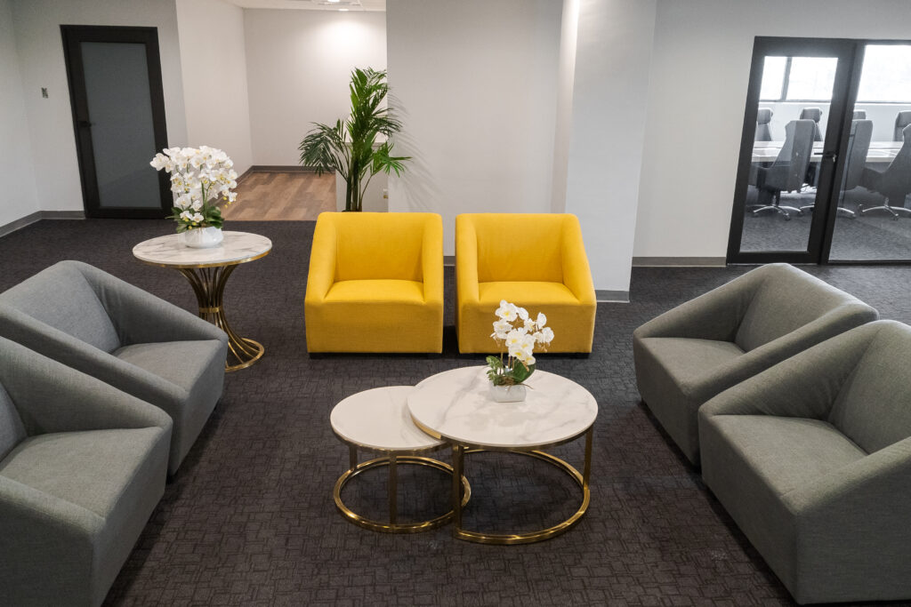 Image inside itel's new Chalmers building in Kingston, Jamaica. One of the intimate gathering areas created on each floor by clusters of modern furnishings, with bright pops of yellow in the chairs, floral accents and marble-accented tables.
